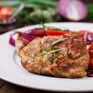 Juicy pork steak with rosemary and tomatoes on a white plate